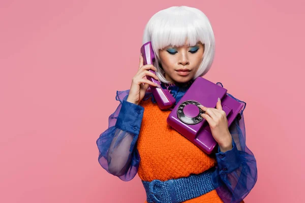 Fashionable asian pop art woman talking on purple telephone isolated on pink — Stock Photo