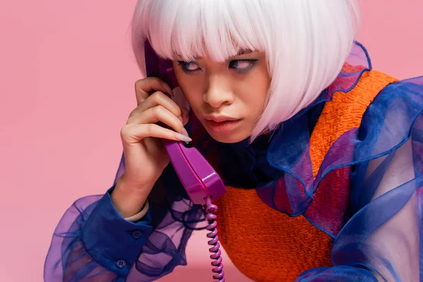 Азиатская модель поп-арта разговаривает по ретро-телефону с кабелем на розовом фоне — стоковое фото