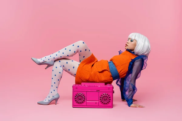 Stylish asian woman in retro dress and white wig posing near boombox on pink background — Stock Photo