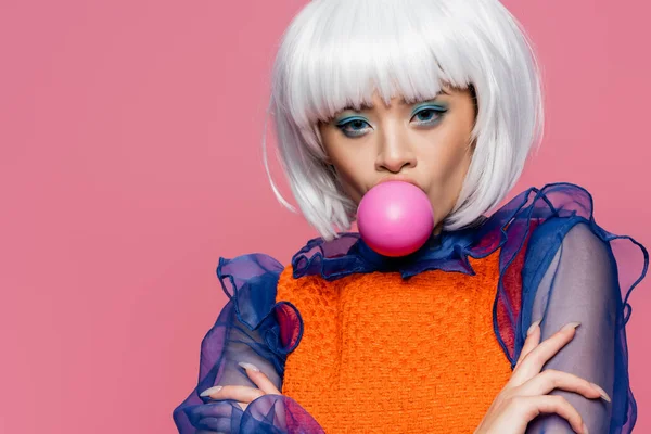 Fashionable asian model blowing bubble gum and looking at camera isolated on pink — Stock Photo