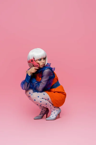 KYIV, UCRANIA - 10 DE DICIEMBRE DE 2020: Mujer de arte pop asiática sosteniendo joystick sobre fondo rosa - foto de stock