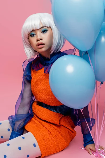 Hübsches asiatisches Pop-Art-Modell mit Blick auf die Kamera in der Nähe von Luftballons auf rosa Hintergrund — Stockfoto