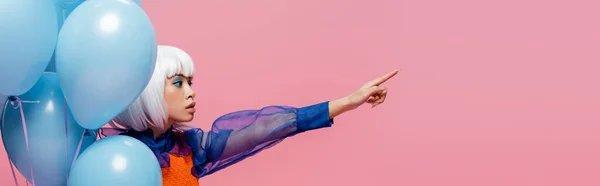 Modelo de arte pop asiático elegante apontando com o dedo perto de balões isolados em rosa, banner — Fotografia de Stock