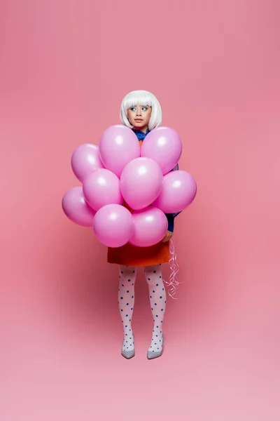 Bastante asiático pop arte modelo en punteado medias celebración globos en rosa fondo - foto de stock