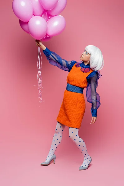 Стильная азиатка в стиле поп-арта смотрит на воздушные шары на розовом фоне — стоковое фото