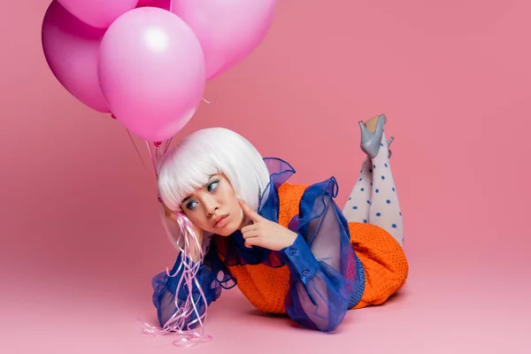 Pensive asiatische Pop Art Frau hält Luftballons, während sie auf rosa Hintergrund liegt — Stockfoto