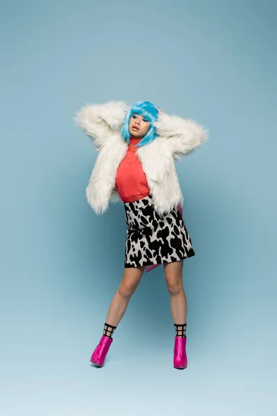 Модна азіатська поп-арт жінка торкається перуки на синьому фоні — стокове фото