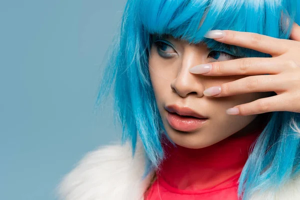 Portrait of young asian woman in wig touching face isolated on blue — Stock Photo