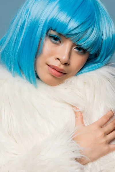Retrato de mujer asiática bonita en peluca brillante y chaqueta peluda aislada en azul - foto de stock