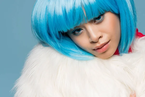 Portrait of young asian woman in wig and furry jacket looking at camera isolated on blue — Stock Photo