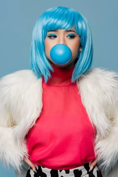 Asiatico donna in peloso giacca soffiando bolla gomma isolato su blu — Foto stock