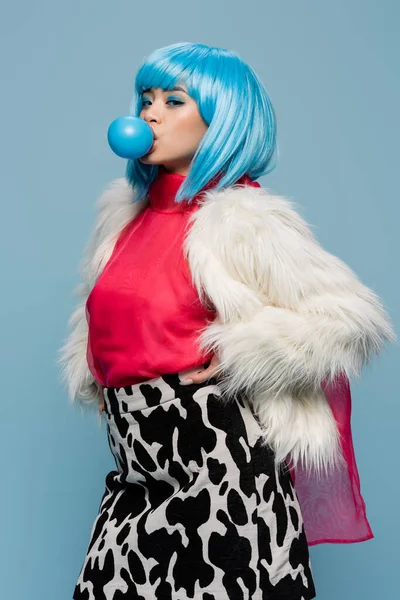 Young asian woman in furry jacket blowing bubble gum isolated on blue — Stock Photo