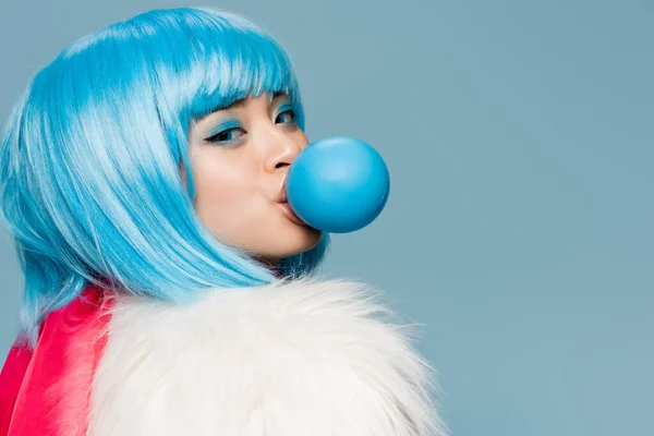 Pretty asian woman in furry jacket blowing bubble gum and looking at camera isolated on blue — Stock Photo