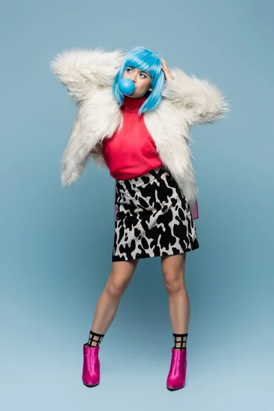 Full length of pop art asian woman blowing bubble gum on blue background — Stock Photo