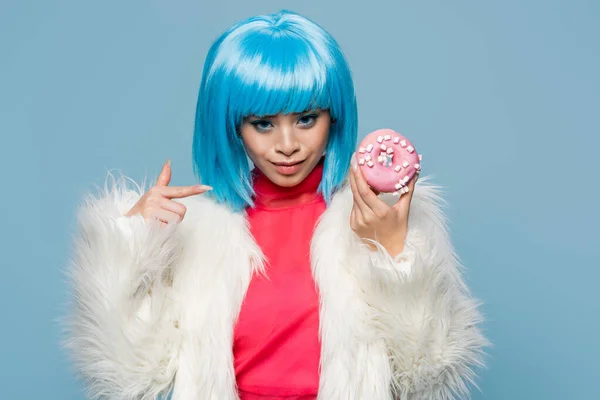 Smiling asian woman in pop art style pointing at donut isolated on blue — Stock Photo