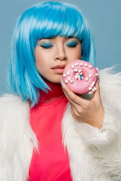 Asian woman in pop art style closing eyes while holding tasty donut isolated on blue — Stock Photo