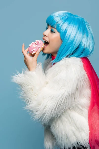 Jeune asiatique pop art femme tenant délicieux beignet près de bouche ouverte isolé sur bleu — Photo de stock