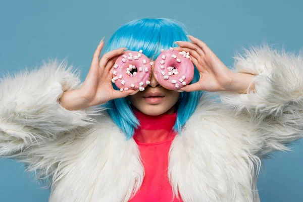 Mulher elegante em peruca brilhante segurando donuts perto do rosto isolado em azul — Fotografia de Stock