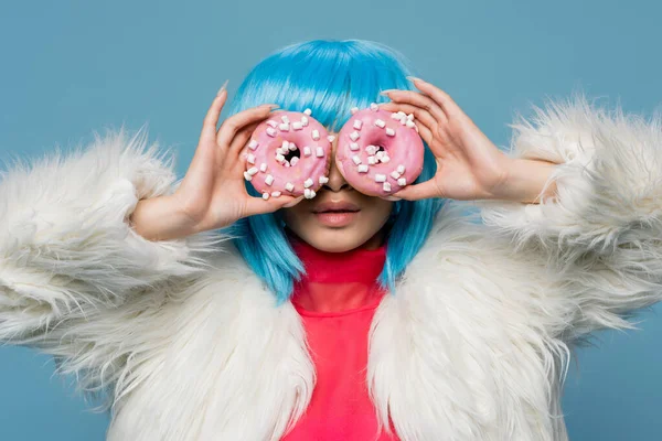 Femme élégante en perruque lumineuse tenant des beignets près du visage isolé sur bleu — Photo de stock