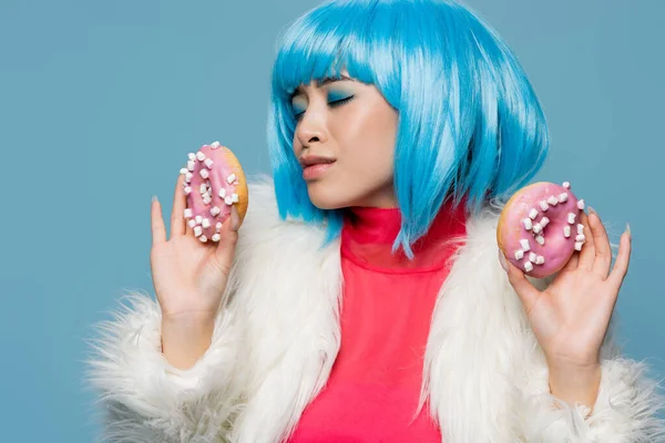 Stylish asian woman in bright wig holding delicious donuts isolated on blue — Stock Photo