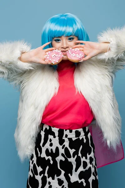 Smiling asian woman in pop art style holding donuts isolated on blue — Stock Photo