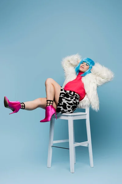 Усміхнена азіатка в стилі поп-арту сидить на білому стільці на синьому фоні — стокове фото