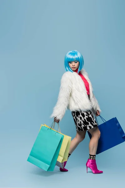 Stylish asian woman in pop art style holding shopping bags on blue background — Stock Photo