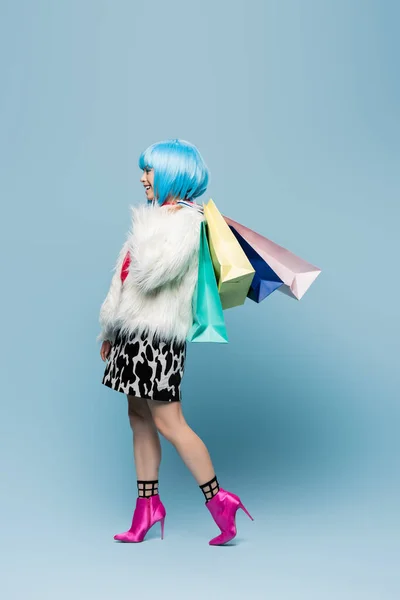 Вид сбоку на женщину в стиле поп-арт, держащую в руках сумки с покупками и улыбающуюся на синем фоне — стоковое фото
