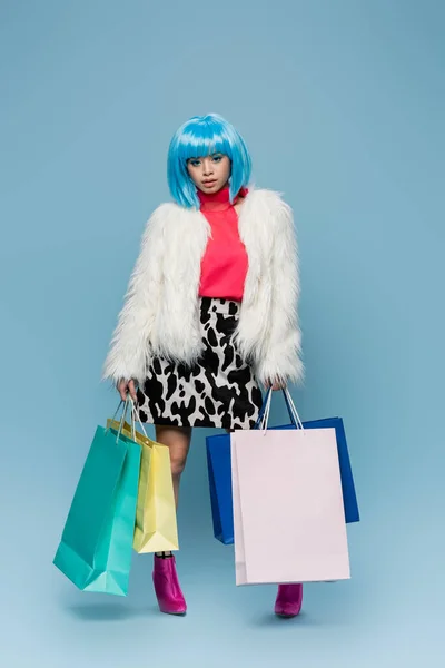 Pretty asian woman in pop art style holding shopping bags on blue background — Stock Photo