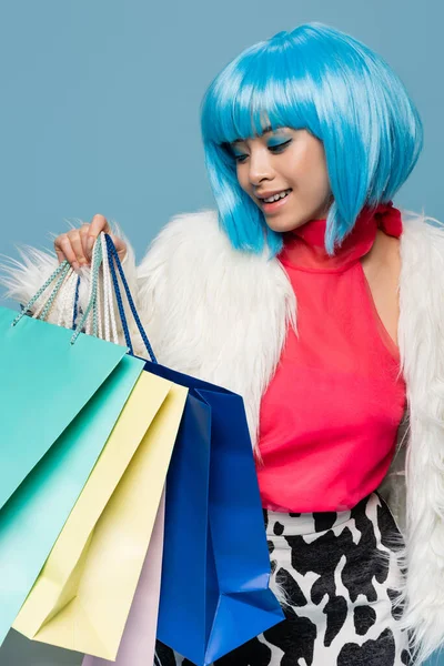 Modelo asiático positivo en estilo pop art sosteniendo bolsas aisladas en azul - foto de stock