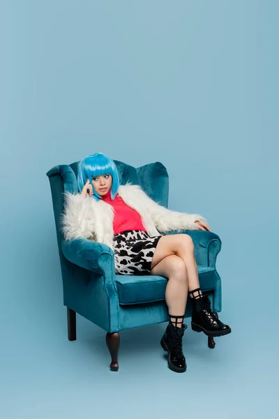Азійка в стилі поп-арту сидить на стільці на синьому фоні. — стокове фото