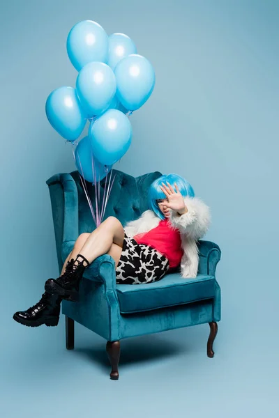 Femme asiatique dans le style pop art tenant des ballons et couvrant le visage avec la main sur fond bleu — Photo de stock