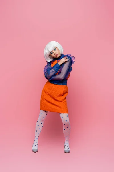 Stylish asian woman in heels and white wig posing on pink background — Stock Photo