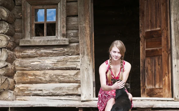 Chica con un perro sentado en la puerta casa de madera — Foto de Stock