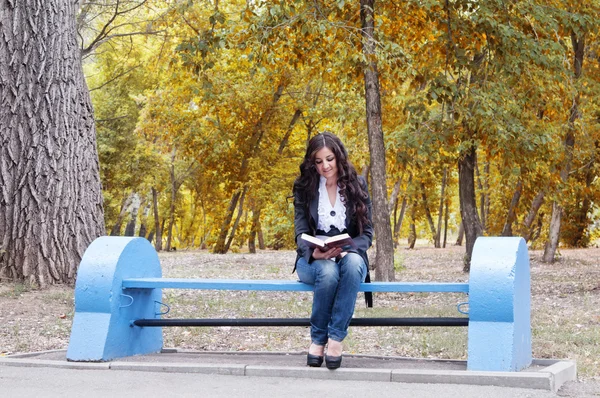 Menina com o livro em um banco no parque de outono — Fotografia de Stock