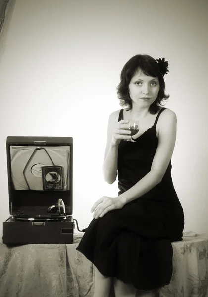 Ragazza con un bicchiere di vino, seduta vicino al grammofono. Vintage . — Foto Stock