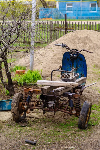 Old broken three-wheeled scooter in the courtyard of a rural house