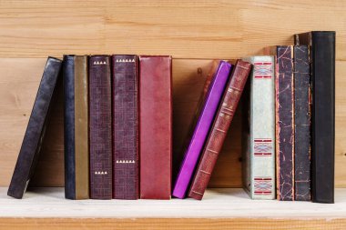 Tahta bir rafta yığınla eski kitap.