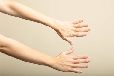 Two human arms and hands reaching forward on beige background, isolated gesture concept.