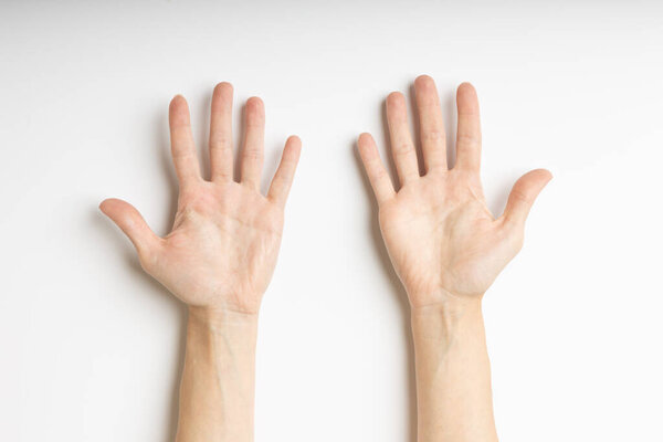 A pair of hands placed on a white surface with palms facing upward and fingers spread open. The lighting is soft and even, highlighting the natural lines and texture of the palms. The composition 