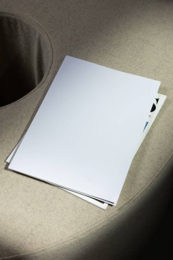 Minimalist mockup composition with a stack of blank white sheets placed on a soft beige textured surface. Subtle natural light creates elegant shadows, giving depth to the image. Ideal for presenting stationery designs, magazine covers.