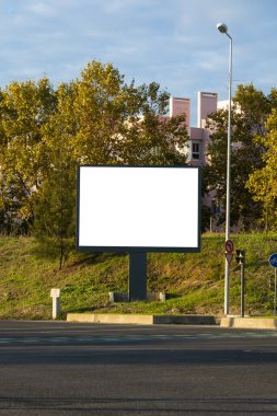 Sessiz bir şehir sokağında, sonbahar ağaçları ve yumuşak akşam ışığında konut binalarıyla çevrili boş bir reklam panosu. Lizbon