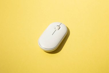 Pürüzsüz, beyaz kablosuz bir bilgisayar faresinin minimalist fotoğrafı canlı sarı bir arka plana yerleştirilmiş. Güçlü renk kontrastı ve yumuşak gölge nesnenin basitliğini ve modern tasarımını vurgular