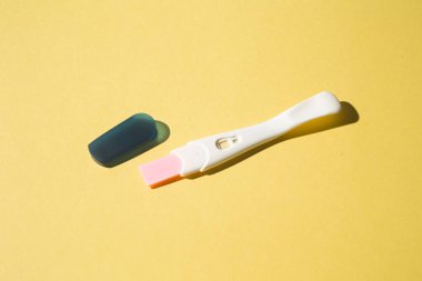 Sarı arka planda hamilelik testi cihazı, erken hamilelik tespiti için kullanılan test setinin yakın çekimini gösteriyor..