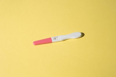 Sarı arka planda hamilelik testi cihazı, erken hamilelik tespiti için kullanılan test setinin yakın çekimini gösteriyor..