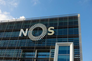 Lisboa, Portekiz 2025-11-14. Büyük NOS logosunun yer aldığı modern cam kaplı bir şirket binası Lizbon 'da açık mavi bir gökyüzünün altında fotoğraflandı..