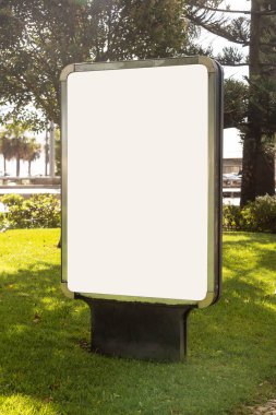 Mockup kentsel reklam panoları, uzun çam ağaçları ve yumuşak öğleden sonra ışıklarıyla çevrili bir yerleşim yerindeki bir yolun yanındaki yaya yolunda duruyor. Boş ekran yüzey vurguları