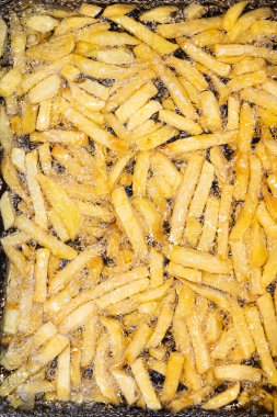 Sıcak yağda kızaran taze patateslerin yakın plan görüntüsü, kızarmış patatesleri çevreleyen altın kabarcıklar. Kıtır kıtır ve altın rengine dönüşmeden önceki anı yakalar..