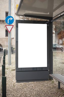 Geleneksel Portekiz kalada kaldırımıyla çevrili büyük boş bir reklam paneliyle modern otobüs durağı. Arka planda trafik işaretleri ve tarihi bir taş binanın bir kısmı görülüyor.