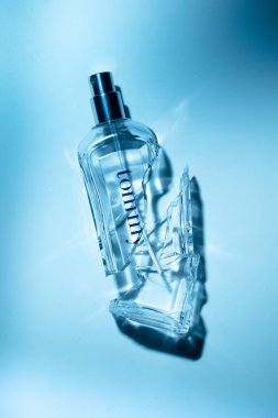 Lizbon, Portekiz 01-21-2026 Kırık bir camın minimalist hayatı Tommy parfüm şişesi keskin gölgeleri mavi arka planda, kırılganlığı, kaybı ve kırık lüksü simgeliyor.